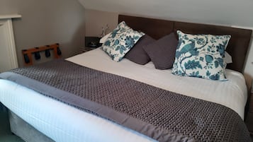 Una cama bien hecha con un edredón marrón y blanco estampado, dos almohadas decorativas con diseño floral azul, y un cabecero de madera.