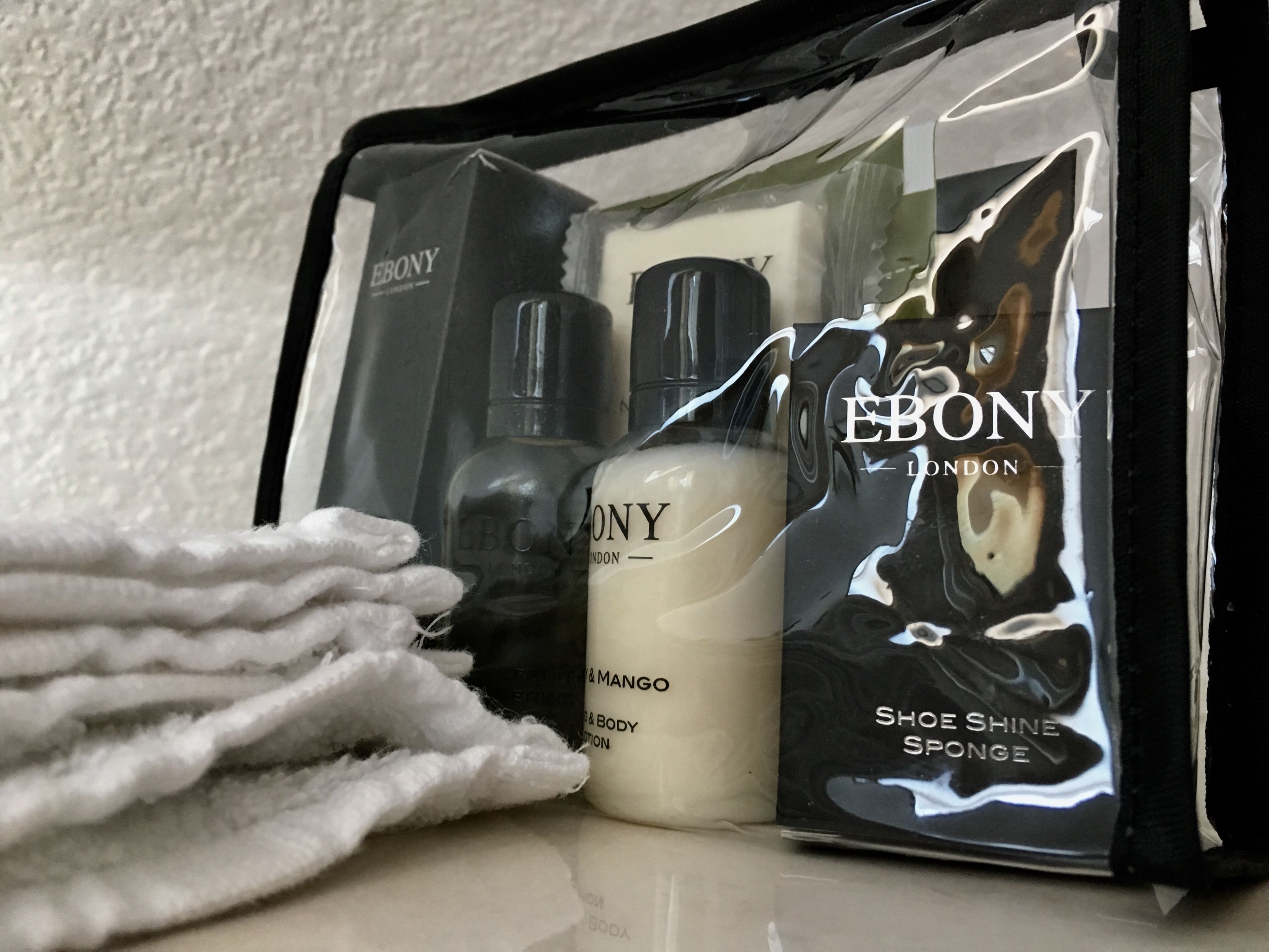 Une trousse de toilette noire contenant un flacon de shampoing, un flacon de lotion pour le corps et un applicateur de crème à chaussures.