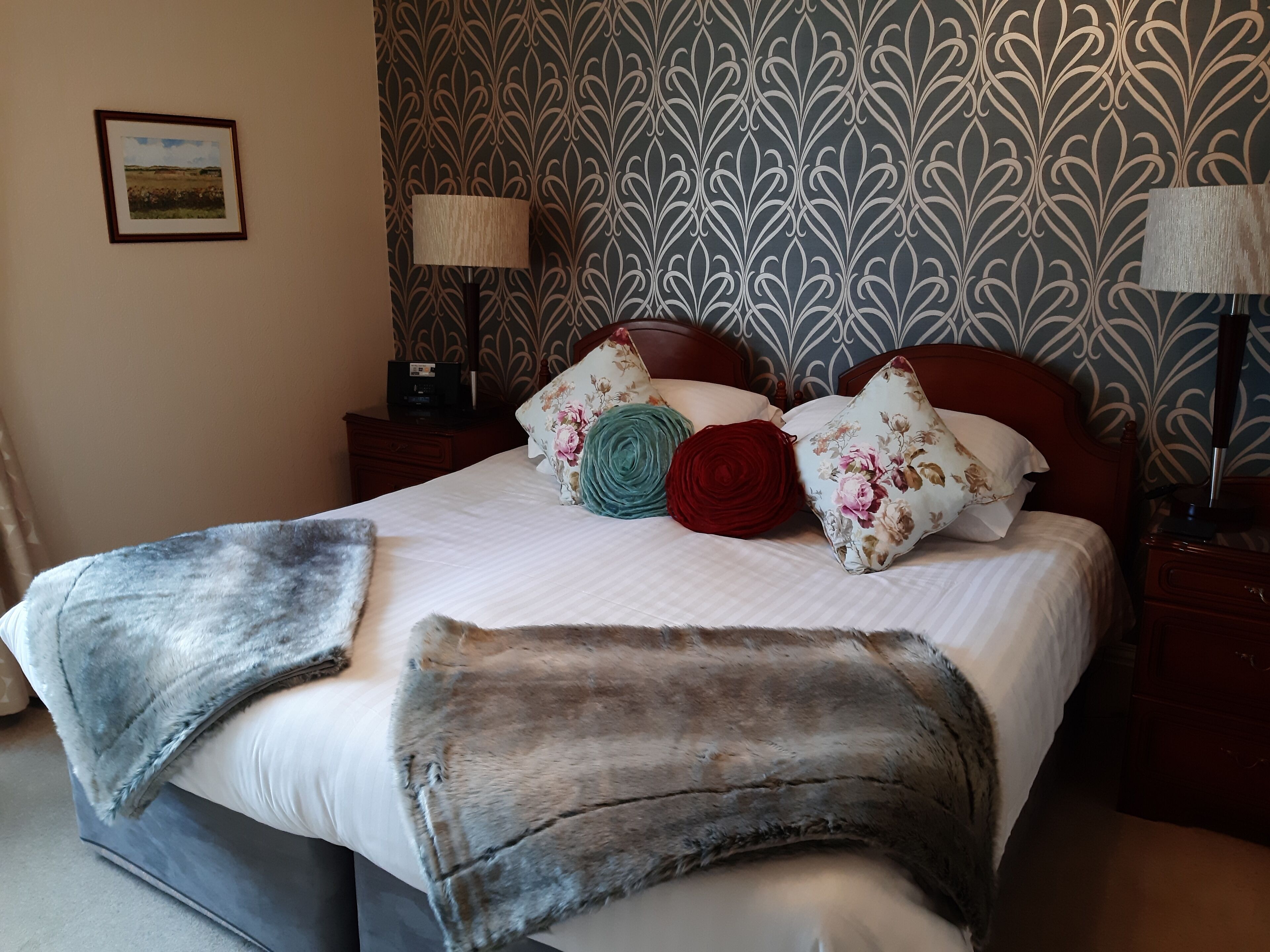Una cama bien hecha con edredón blanco, varios almohadones y una manta gris.