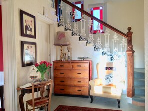 A staircase with ornate white railings and a wooden handrail, leading to a room with a wooden dresser, a chair, and a vase of tulips. - The Spindrift Guest House (Anstruther)