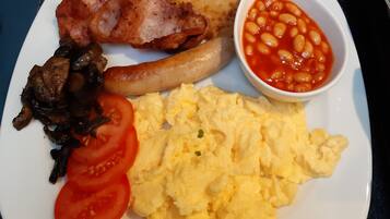 Un plato con huevos revueltos, tocino, salchichas, champiñones, tomates, tostadas y frijoles horneados.
