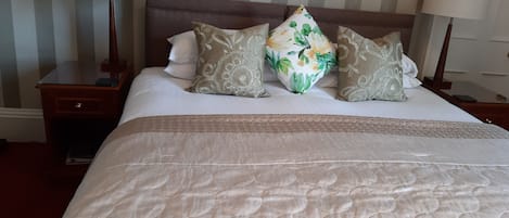 A neatly made bed with a quilted headboard, two bedside tables with lamps, and a striped wall in the background.