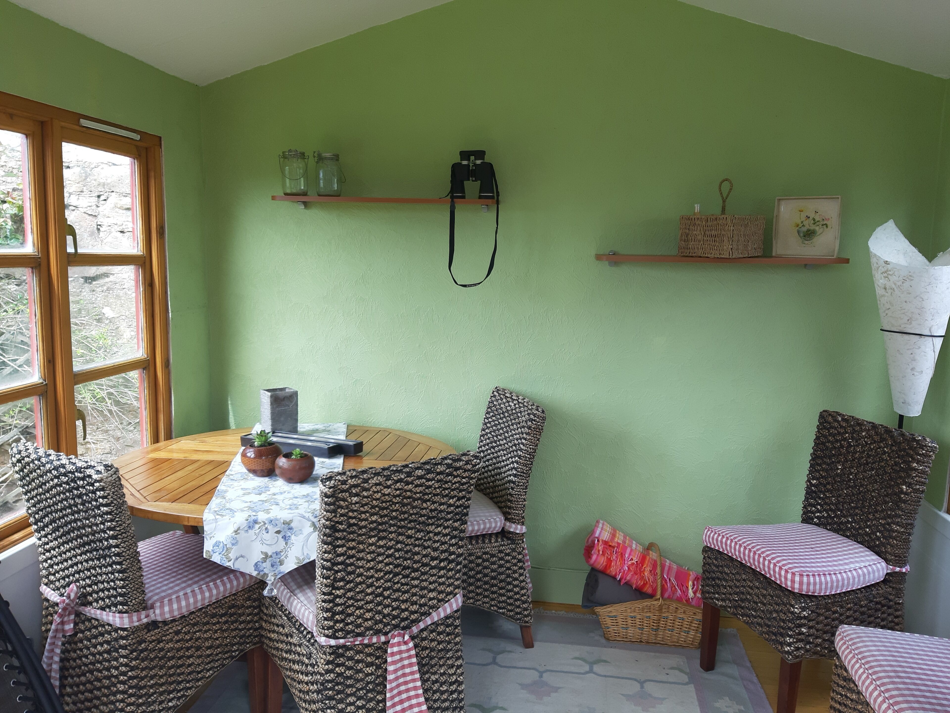 A dining area with a round wooden table, wicker chairs with striped cushions, and a green wall.