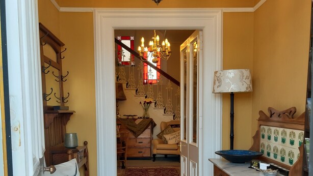 A hallway with a patterned rug, a chandelier, a lamp, and a wooden cabinet with a bowl. - The Spindrift Guest House (Anstruther)