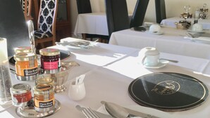 A table set for dining with a black plate, silverware, and three jars of marmalade. - The Spindrift Guest House (Anstruther)