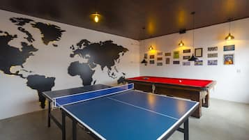 Uma mesa de ping pong, um mapa-múndi na parede, uma mesa de bilhar e luminárias penduradas.