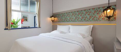 A neatly made bed with white linens, a window with curtains, and a floral-patterned wall above the bed.
