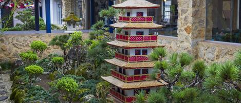 A multi-tiered pagoda-style structure surrounded by a landscaped garden with various plants and rocks.