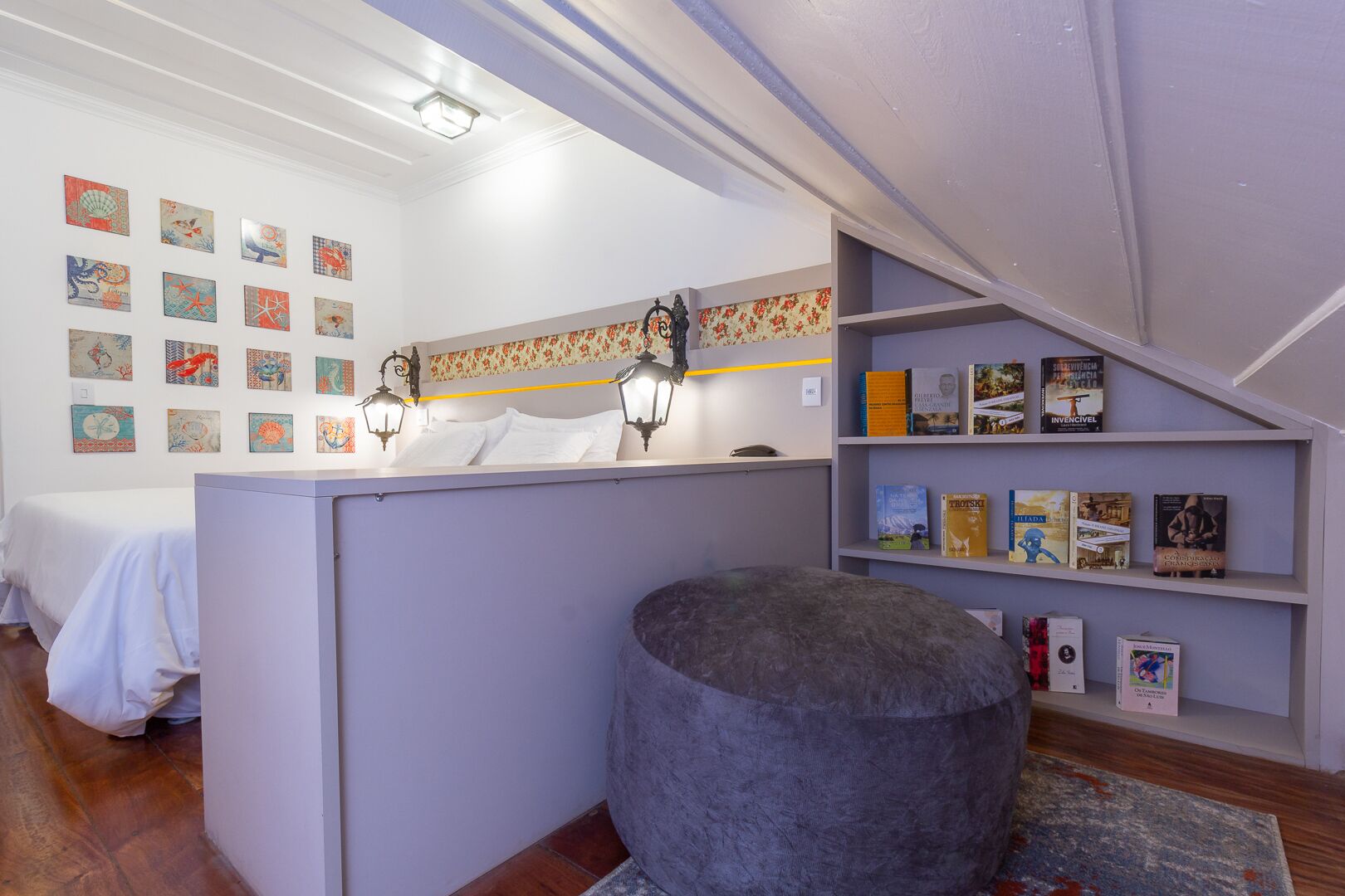 A room with a bed, a desk with a computer, a bookshelf, and various wall art.