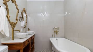 A bathroom with a freestanding bathtub, two sinks with gold fixtures, and a large mirror with ornate gold detailing.