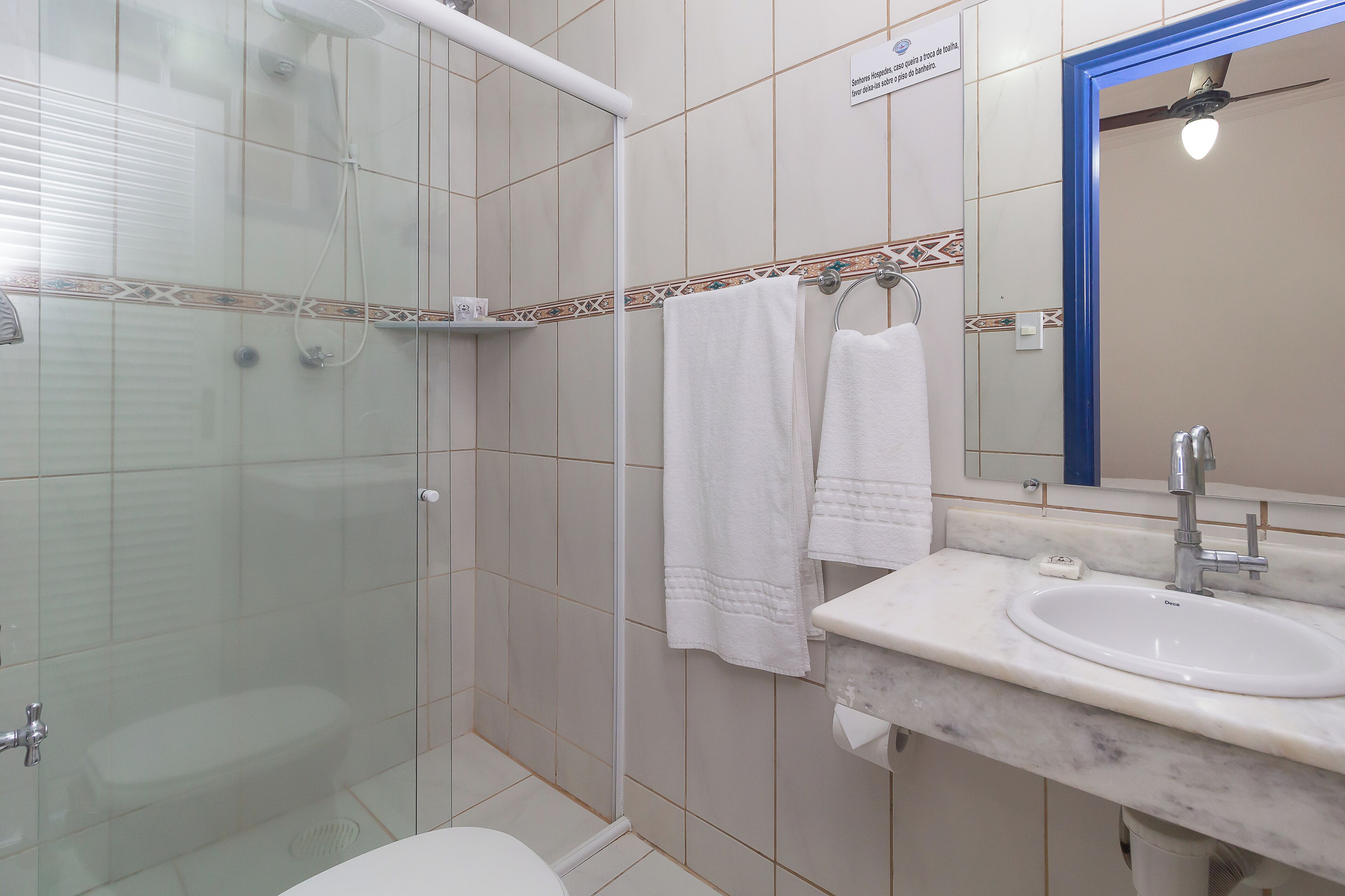A bathroom with a glass-enclosed shower, a toilet, a sink with a marble countertop, and a mirror with a blue frame.