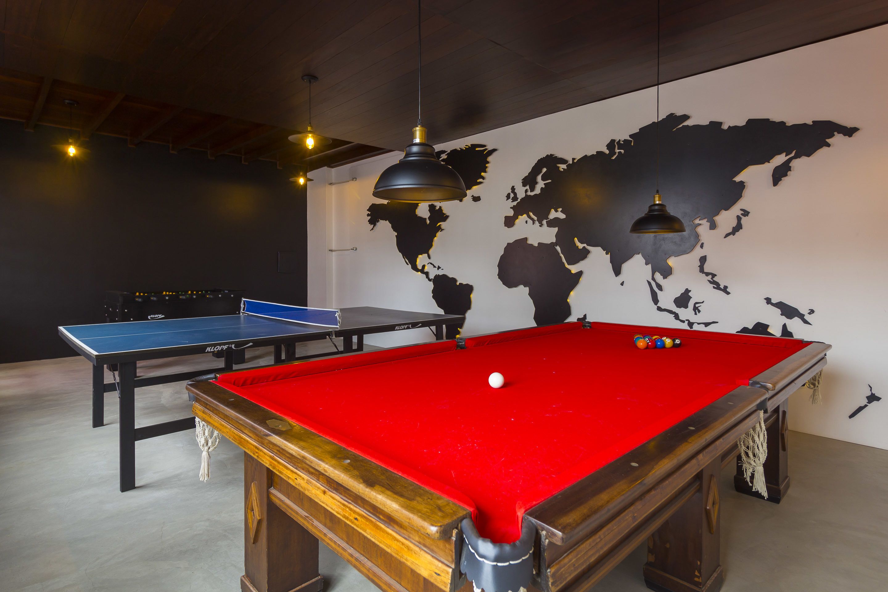 A billiards room with a red pool table, a blue table tennis table, and a world map on the wall.