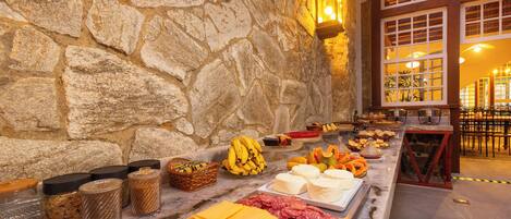 Un mur de pierres sur lequel est disposée une table de buffet présentant des fromages, des charcuteries et des fruits.