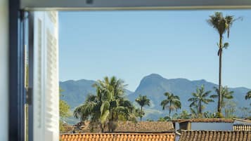 A view through a window of a building with a tiled roof, palm trees, and mountains in the background.