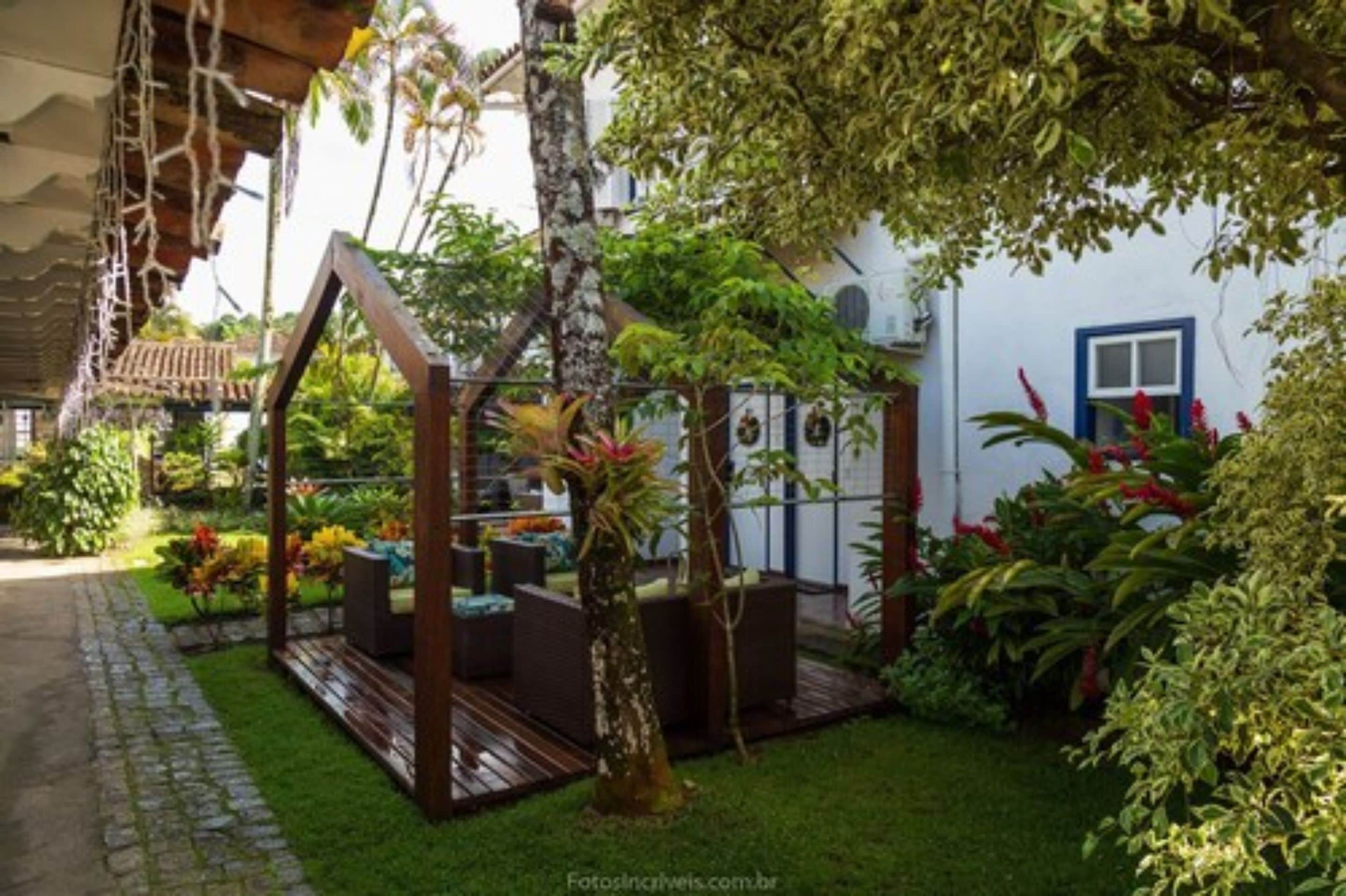Un jardín con un pérgola de madera, un pequeño espacio de estar y diversas plantas.