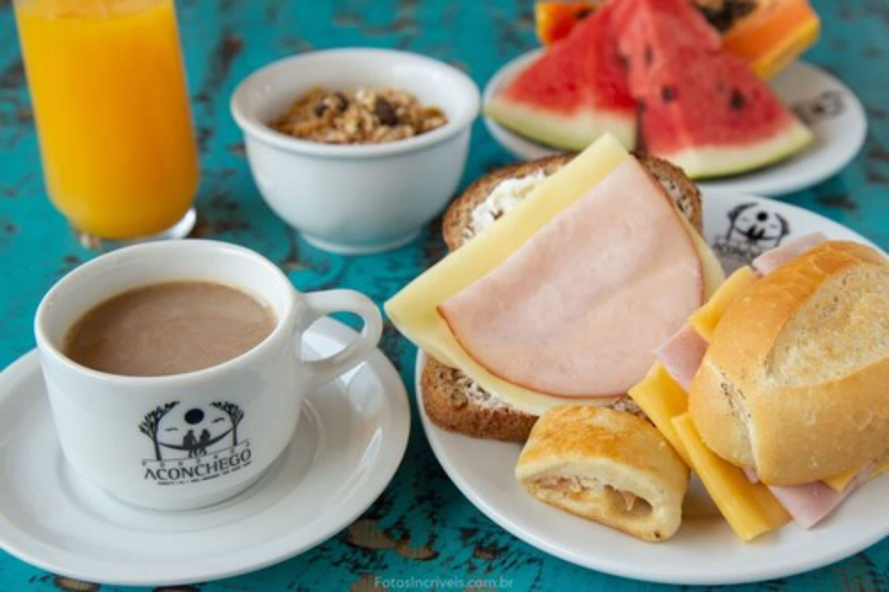 A breakfast setting with a cup of coffee, a plate of sandwiches, a bowl of cereal, and a glass of orange juice.