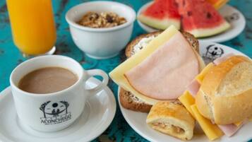 A breakfast setting with a cup of coffee, a plate of sandwiches, a bowl of cereal, and a glass of orange juice.