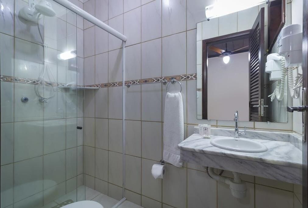 Un baño con cabina de ducha de vidrio, un lavabo con espejo y un perchero para toallas.