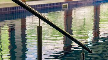 A swimming pool with clear water, metal railings, and a tiled floor.