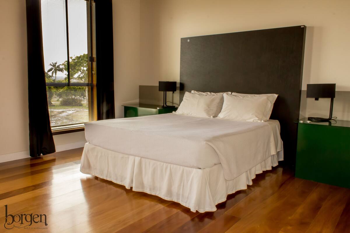 A neatly made bed with a white bedspread and pillows, positioned between two green nightstands with black lamps.