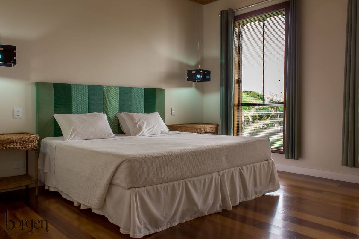 A neatly made bed with a green headboard, a bedside table, and a window with blinds.
