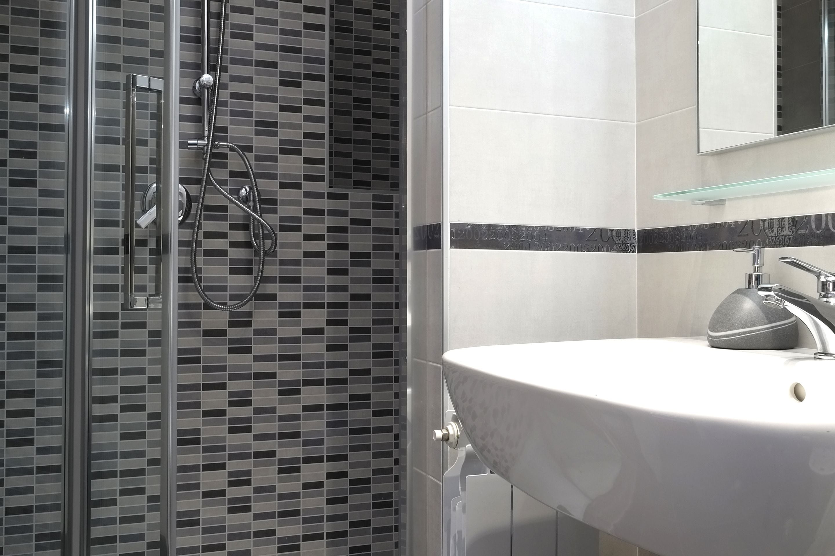 A modern bathroom with a glass shower enclosure, a white sink with a marble countertop, and a mirror above the sink.