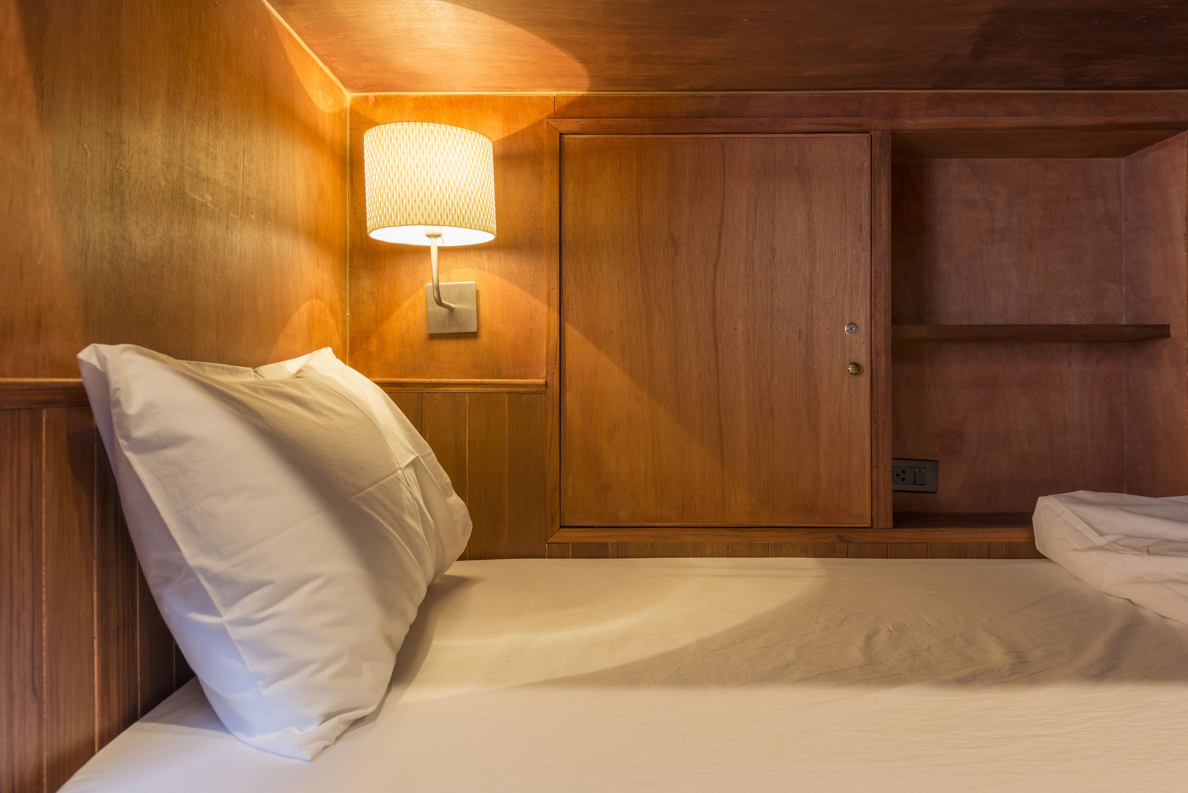 Een houten kamer met een bed, nachtkastje, lamp en garderobe.