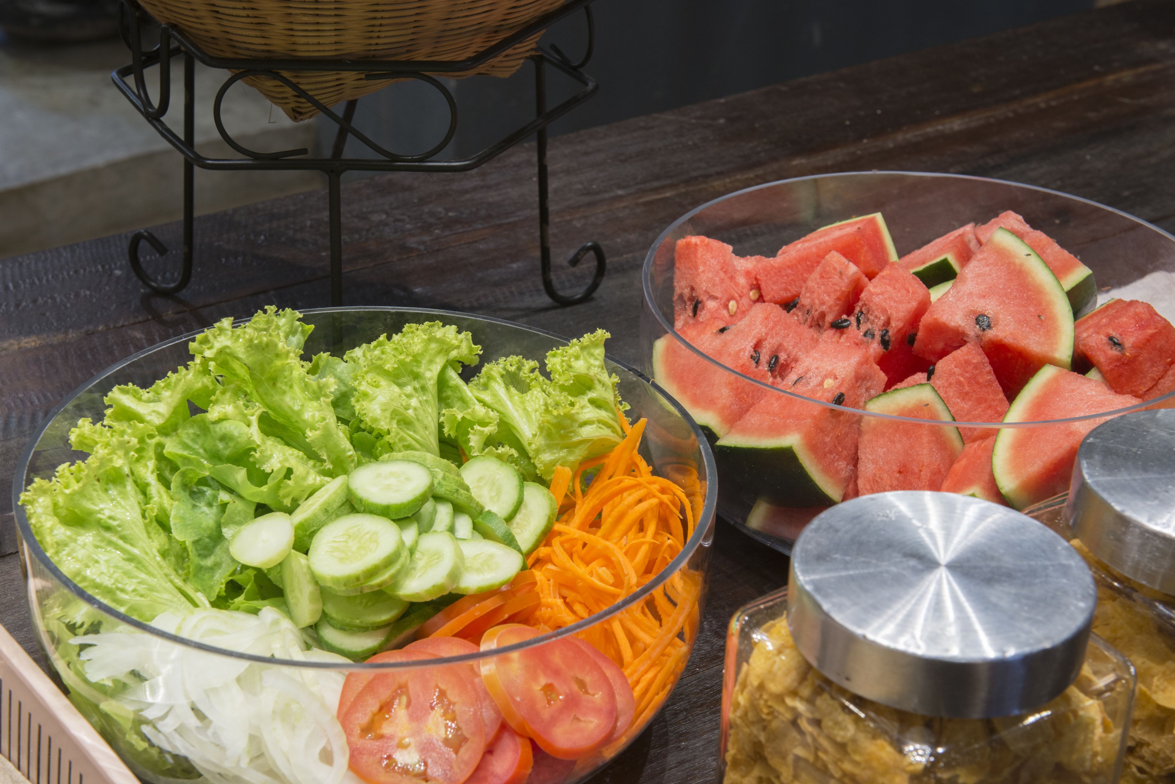 Een buffettafel met een saladeschaal, plakjes watermeloen en potten met sauzen.