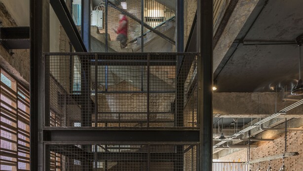 Ein mehrgeschossiges Interieur mit einem zentralen, offenen Bereich, Metallgeländern und einer Backsteinwand.