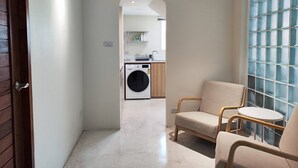 A hallway with a washing machine, a chair, and a table.