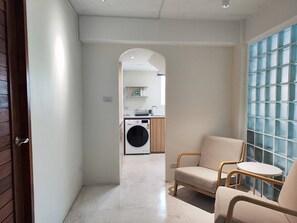 Un couloir avec un lave-linge, une chaise et une table.