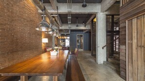 Ein geräumiger Innenraum im Industriedesign mit freiliegenden Backsteinwänden, einem langen Holztisch und hängenden Pendelleuchten.