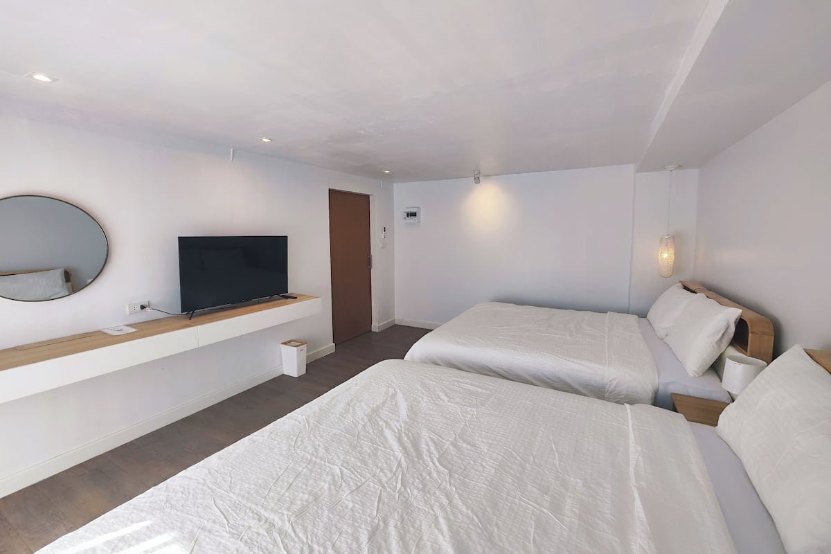 Een moderne hotelkamer met twee bedden, een televisie, een spiegel en een klein nachtkastje.