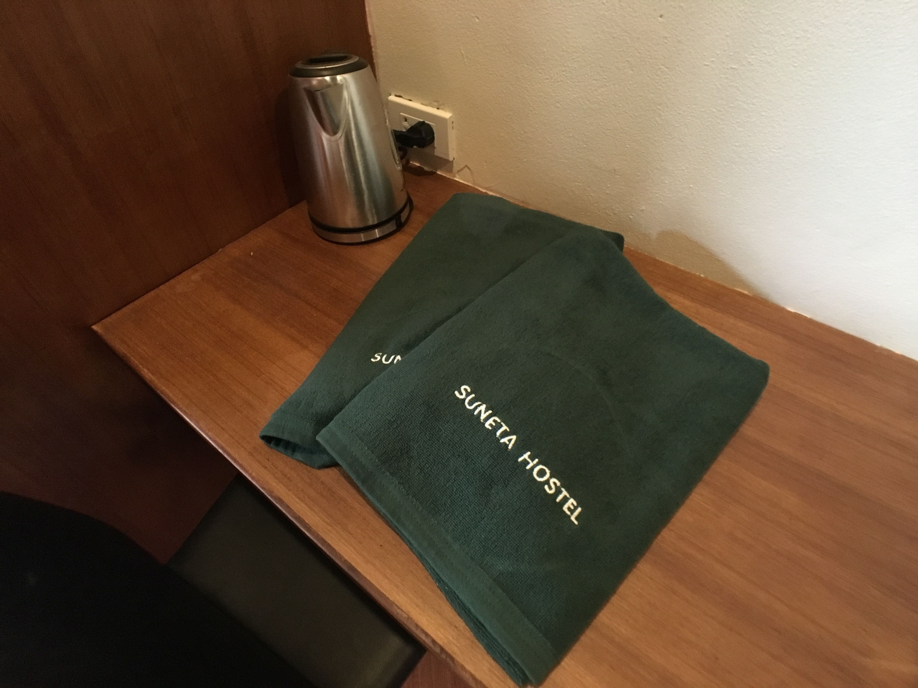 A wooden table with a green towel and a stainless steel kettle.