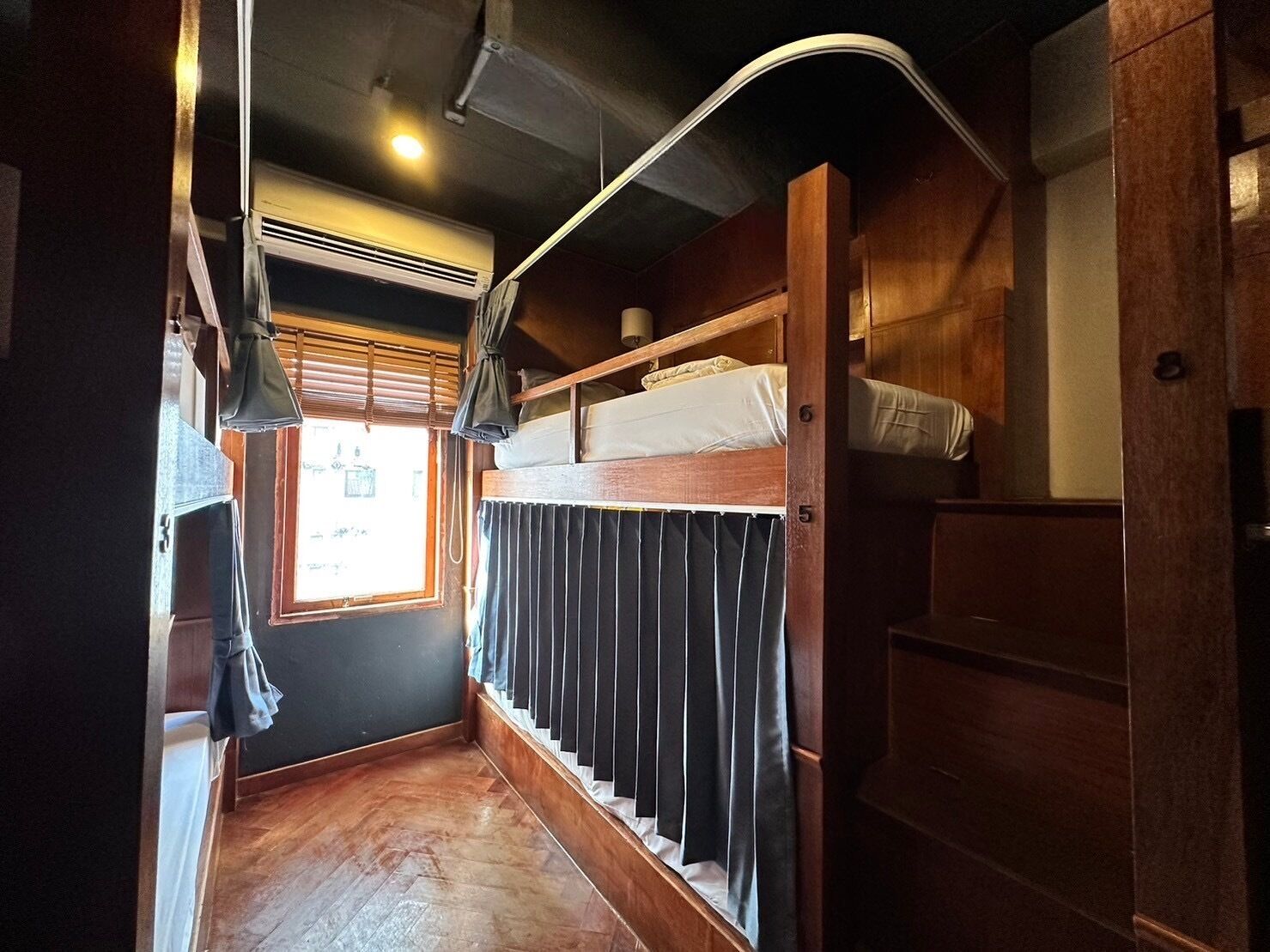 A narrow hallway with a bunk bed, wooden walls, a window with blinds, and a ceiling fan.