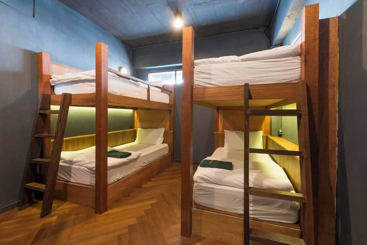 Een studentenkamer met stapelbedden, houten trappen en een visgraat parketvloer.