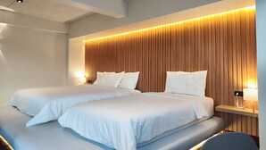 A hotel room with two beds, a wooden headboard, bedside tables with lamps, and a modern ceiling design.