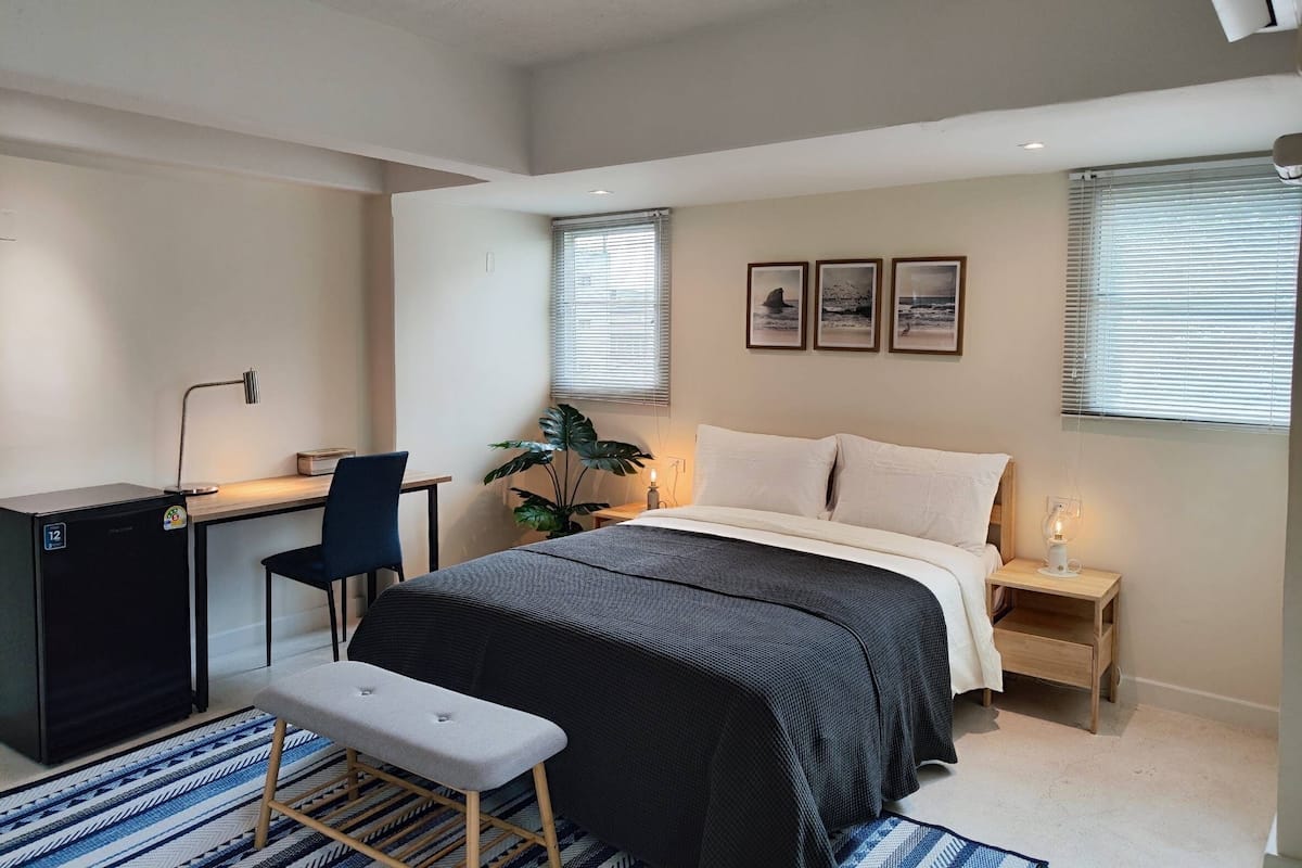 Een moderne slaapkamer met een bed, bureau, stoel en een kleine tafel met een lamp.