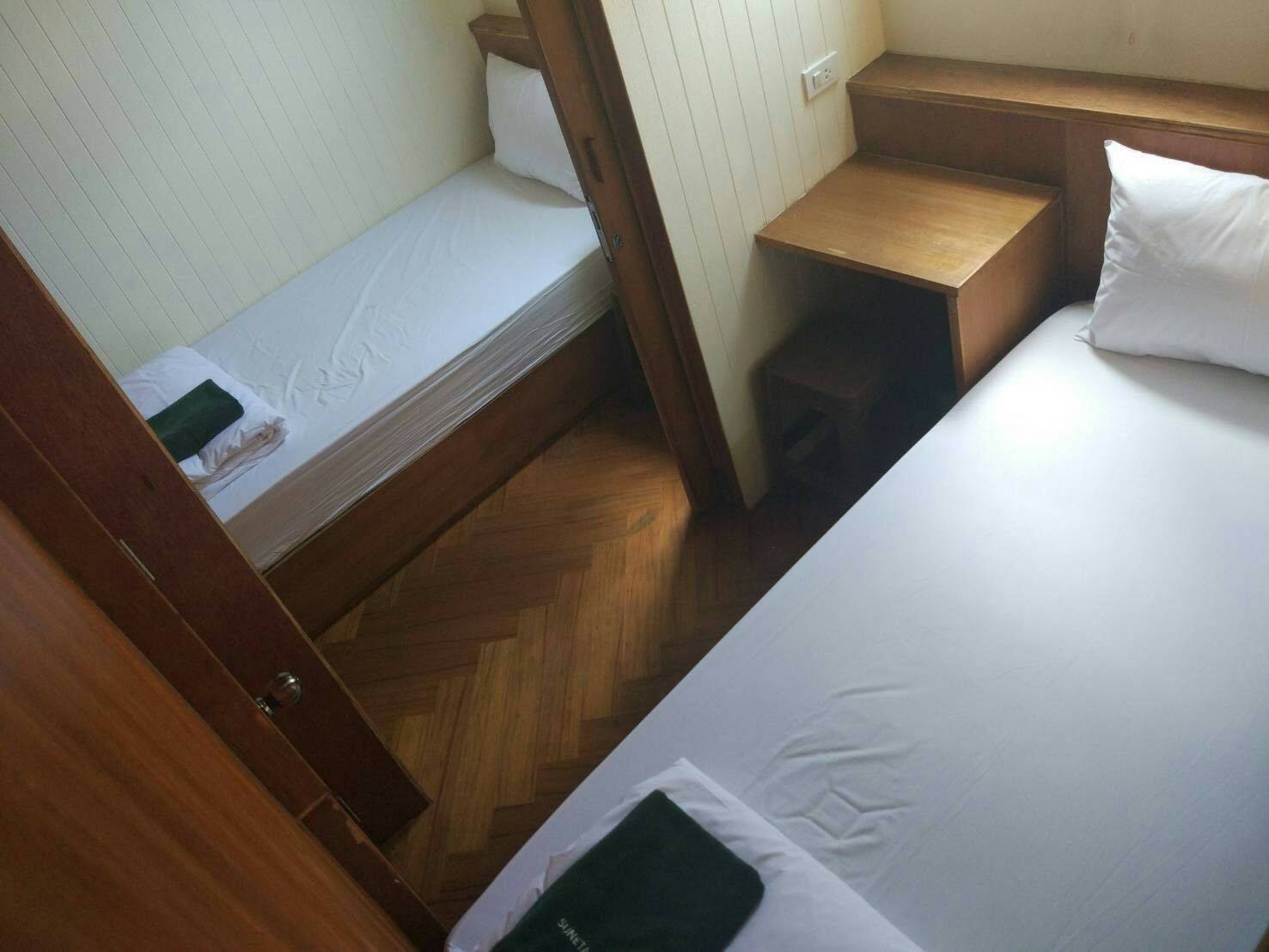 Een kleine, compacte kamer met twee bedden, houten vloeren en een klein houten krukje.