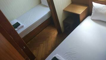 A small, compact room with two beds, wooden flooring, and a small wooden stool.