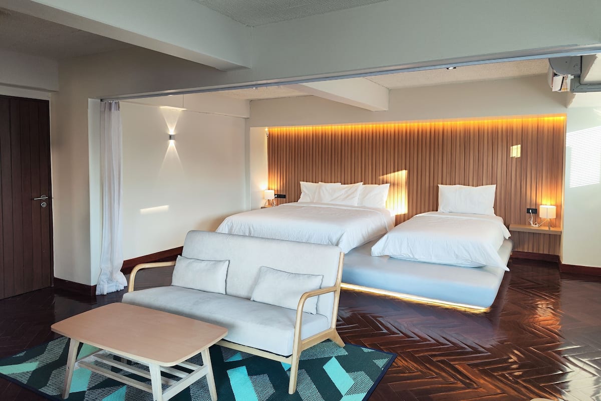Een hotelkamer met twee bedden, een bank, een tafeltje en een visgraatvloer.