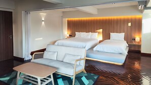A hotel room with two beds, a sofa, a small table, and a herringbone-patterned floor.