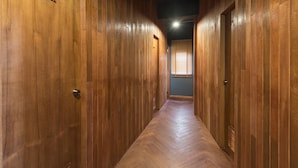 A hallway with wooden paneling and numbered doors, leading to a room with a window and blinds.