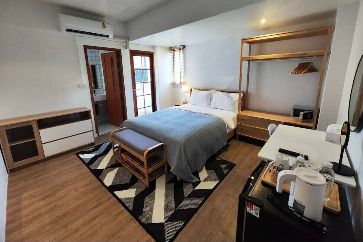 Een moderne slaapkamer met een bed, nachtkastje, bankje en een kleine kitchenette.