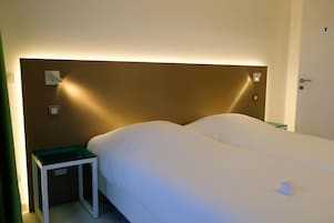 Una habitación de hotel con una cama individual, una mesita de noche y un velador.