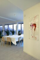 A modern dining area with a white table set for six, surrounded by potted plants and large windows.