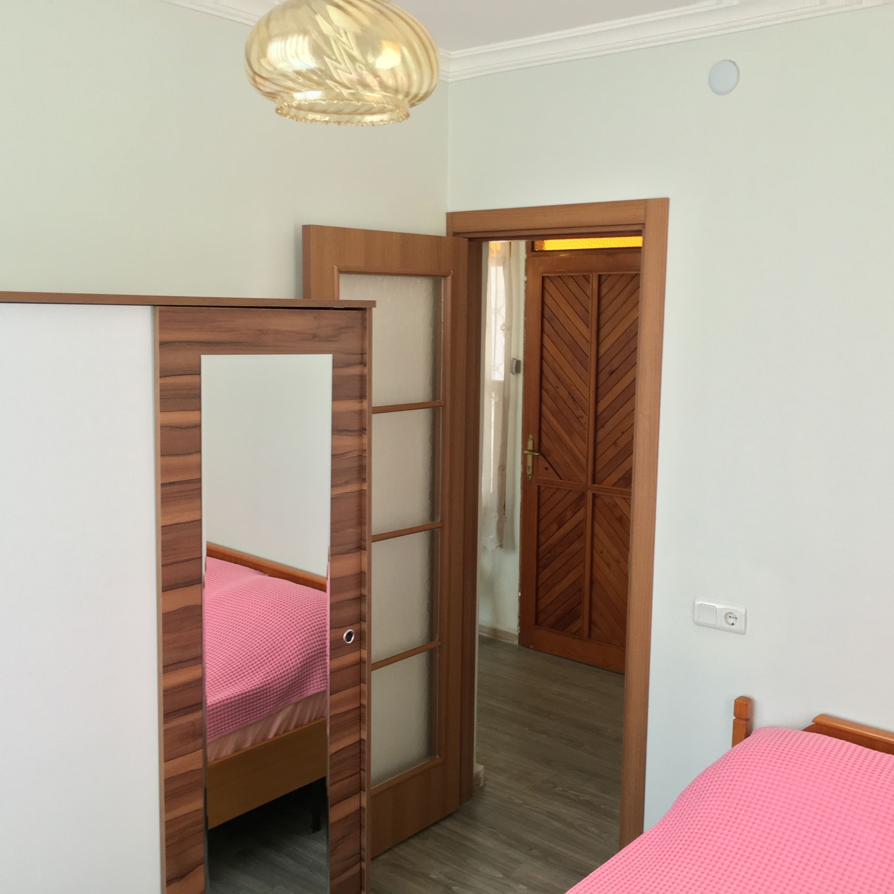 A bedroom with a bunk bed, a wooden wardrobe, and a door leading to another room.