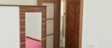 A bedroom with a bunk bed, a wooden wardrobe, and a door leading to another room.