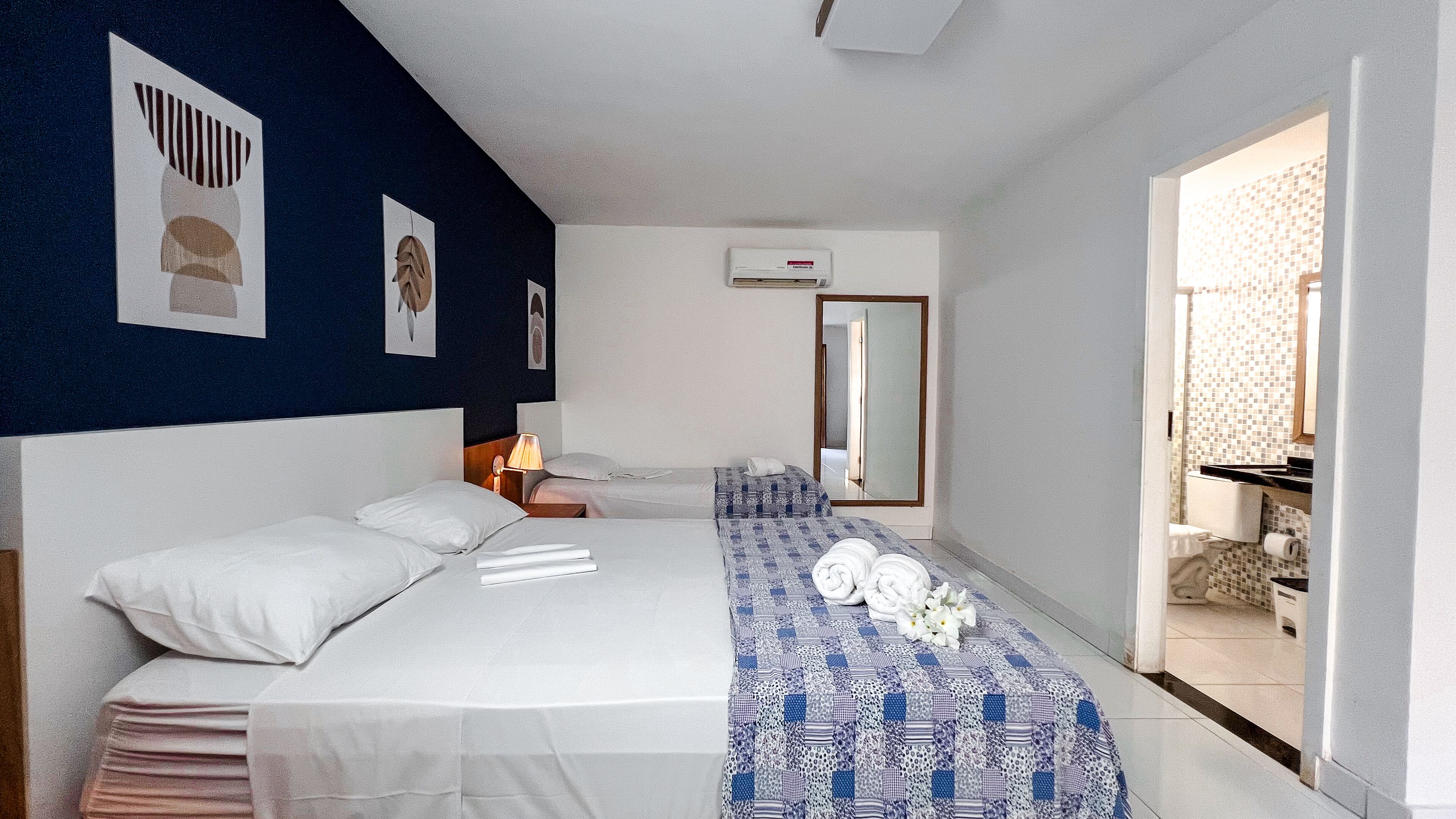 A hotel room with a large bed, a bedside table, a lamp, a mirror, and a bathroom visible through an open door.