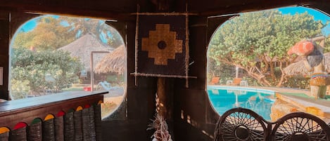 A room with a large window overlooking a pool and outdoor area, a wooden bar with colorful bottles, and a hanging decoration.